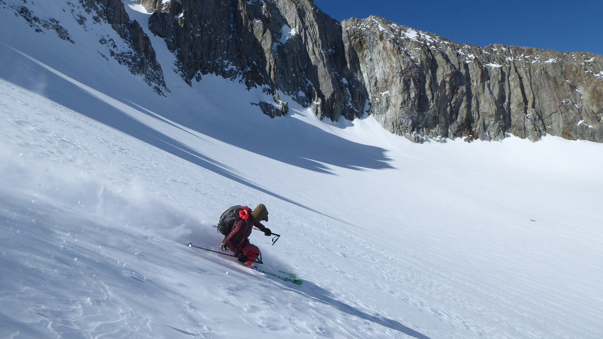 Skieur en pleine descente dans la poudreuse au pied de falaises rocheuses