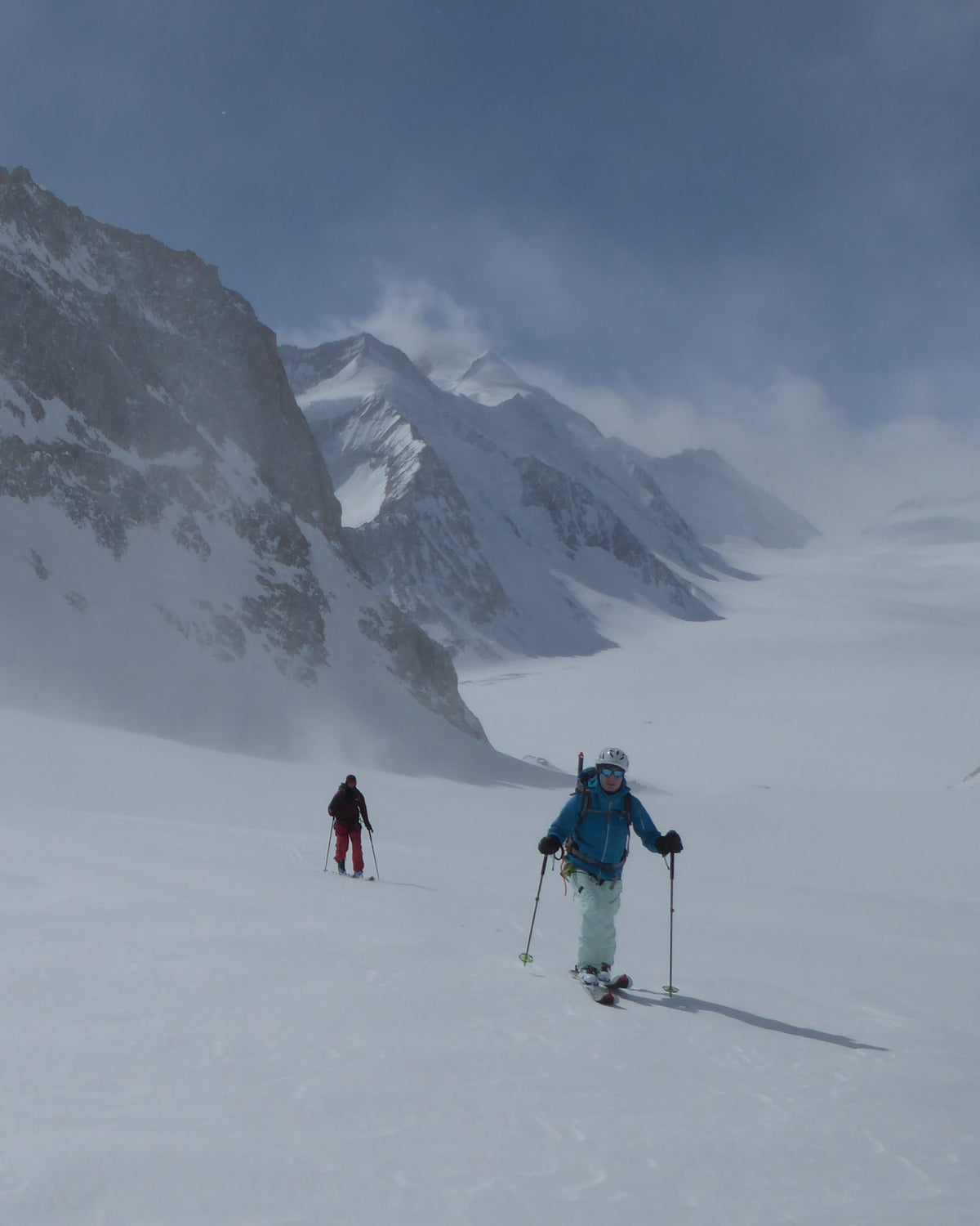 Deux skieurs de randonnée en montée dans la brume au pied de parois
