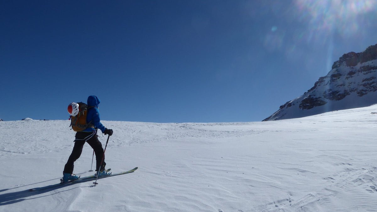 Skieur de randonnée en montée sous un ciel bleu intense