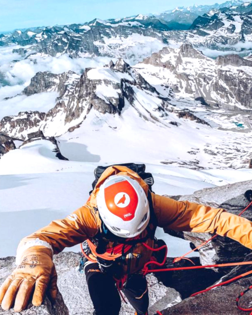 Alpiniste casqué en pleine progression sur un rocher, glaciers en contrebas