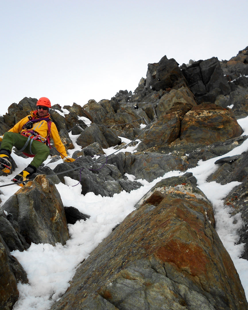 Alpiniste encordé en progression sur une arête rocheuse partiellement enneigée