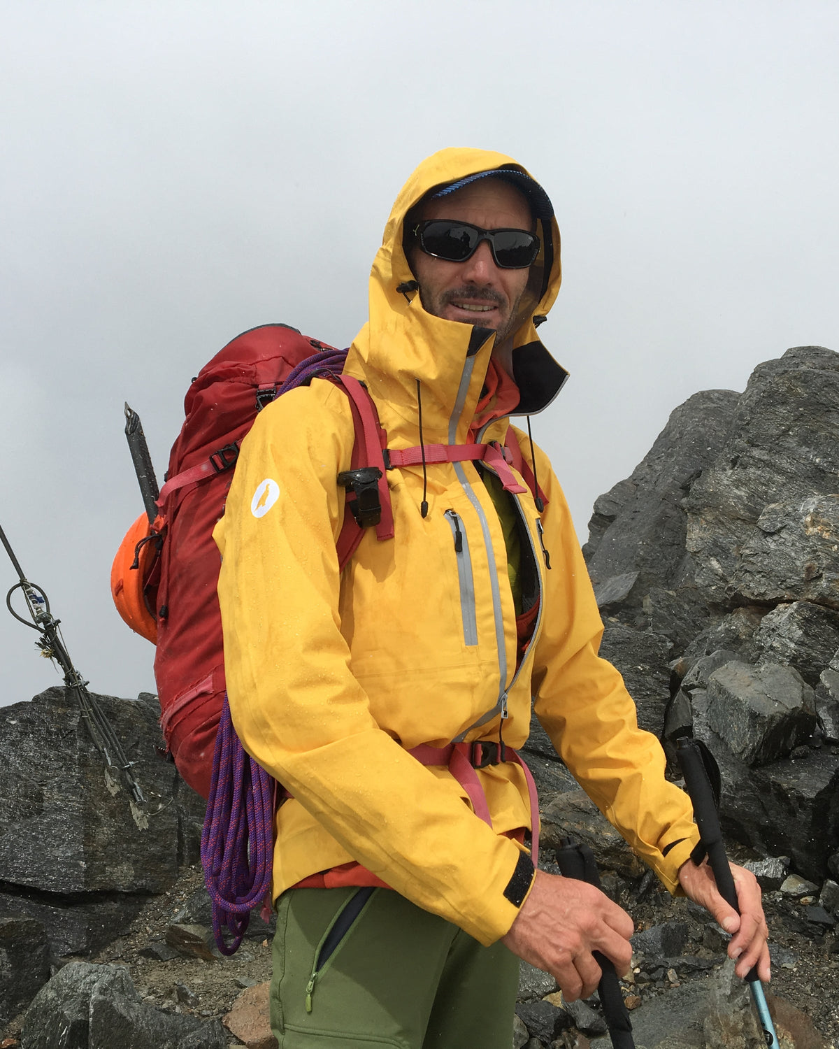 Alpiniste en veste jaune à capuche près d'un relais rocheux en haute montagne