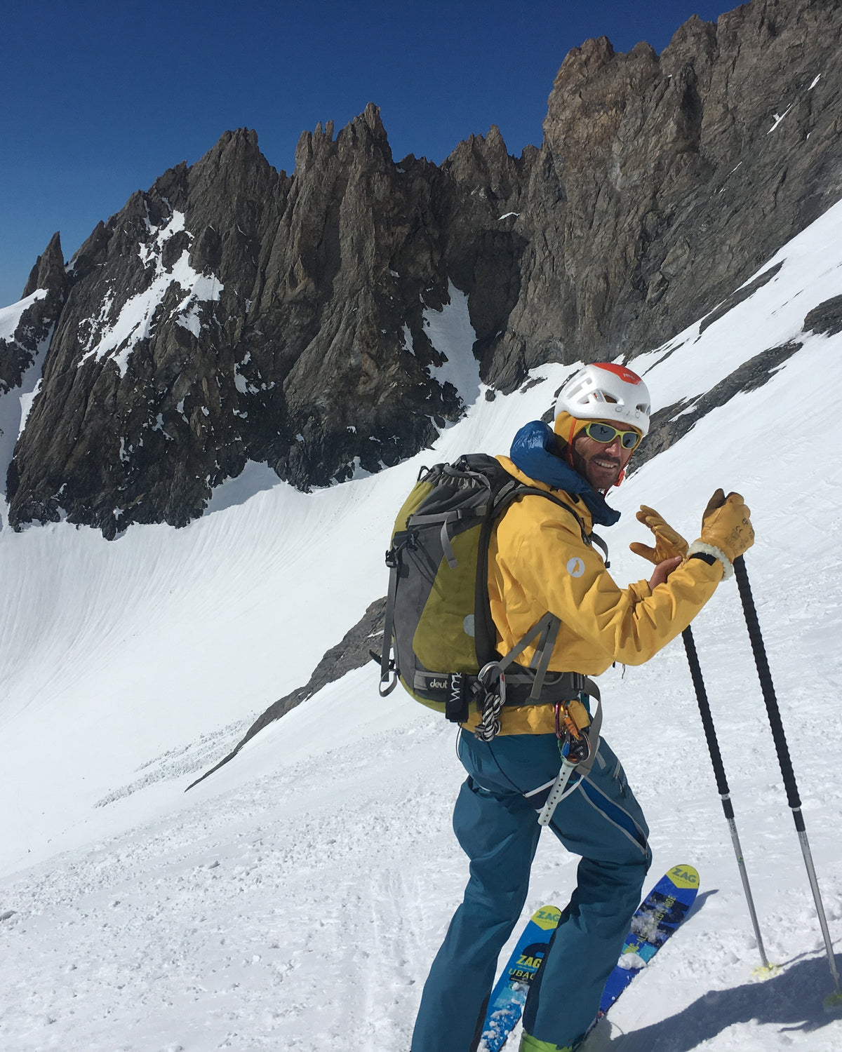 Skieur en veste jaune, bâtons en main, au pied d'aiguilles rocheuses