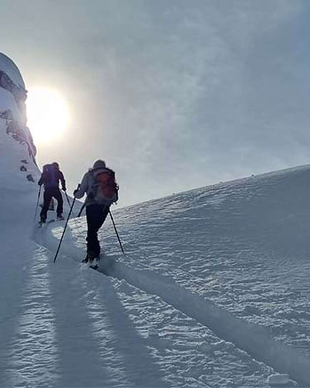 Cordée de skieurs de randonnée à contre-jour sur une trace de montée