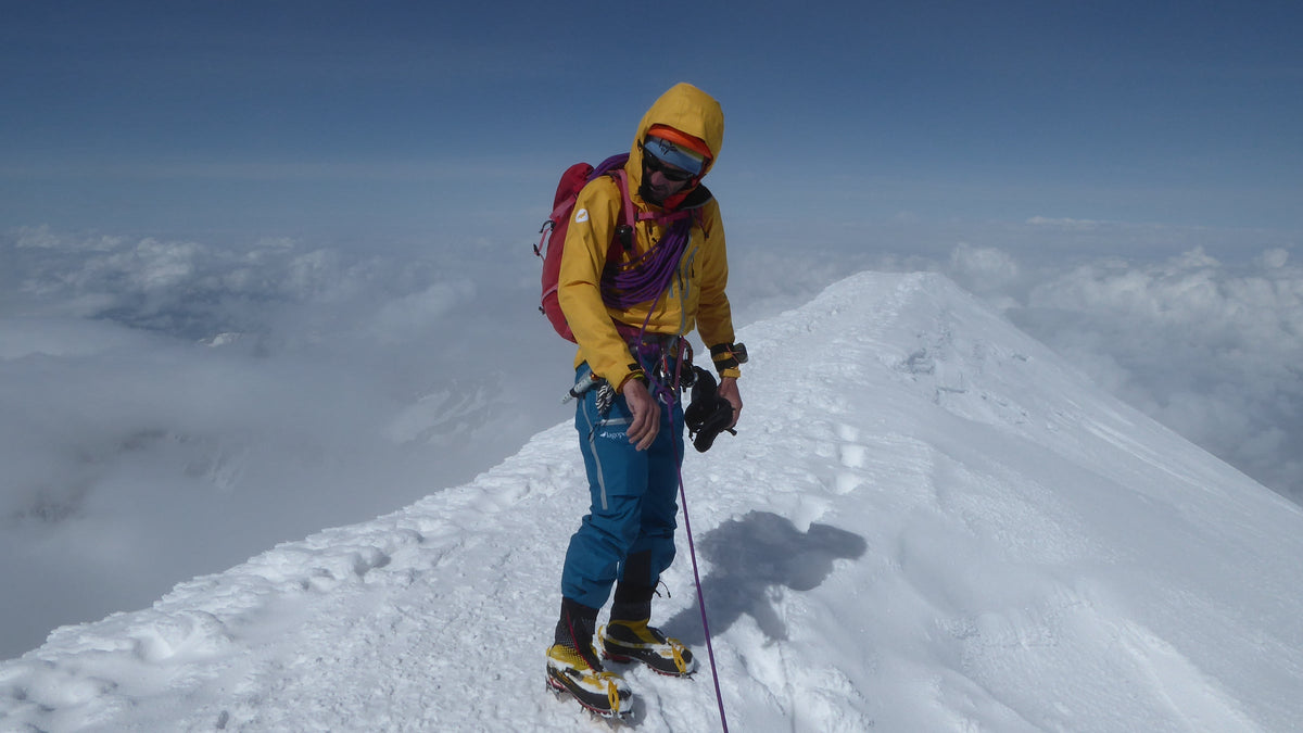 Alpiniste souriant au sommet enneigé, au-dessus d'une mer de nuages