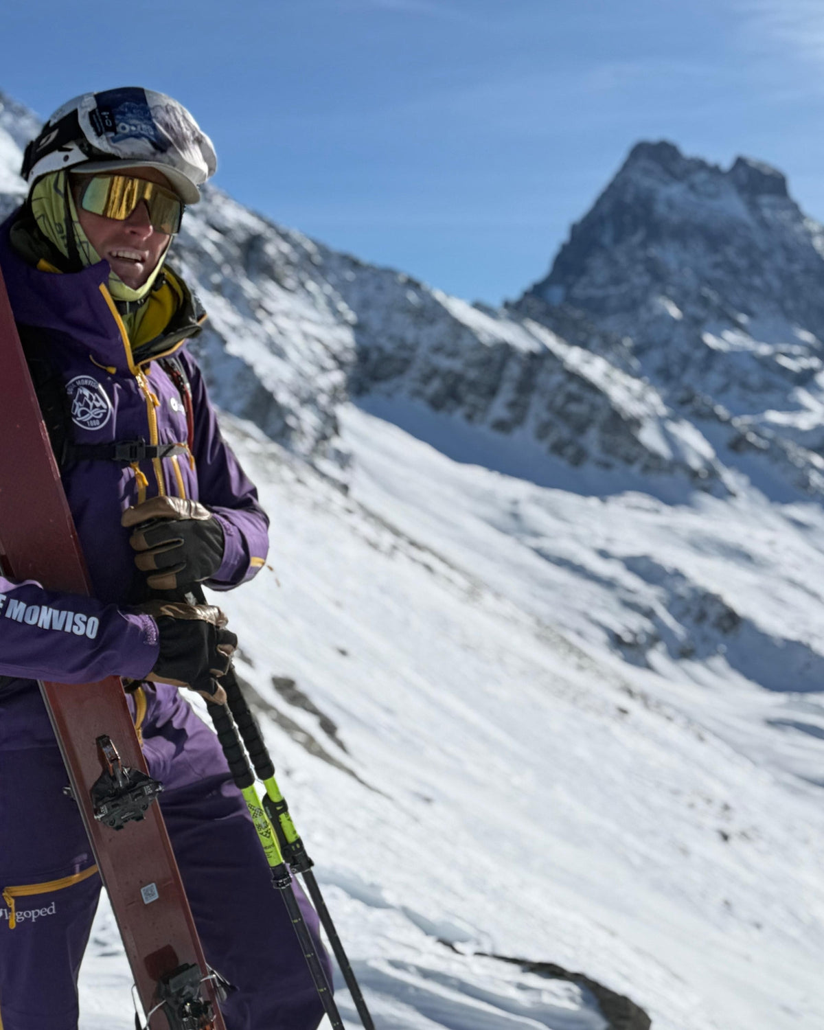 Skieur-alpiniste casqué, skis sur le sac, devant un sommet enneigé