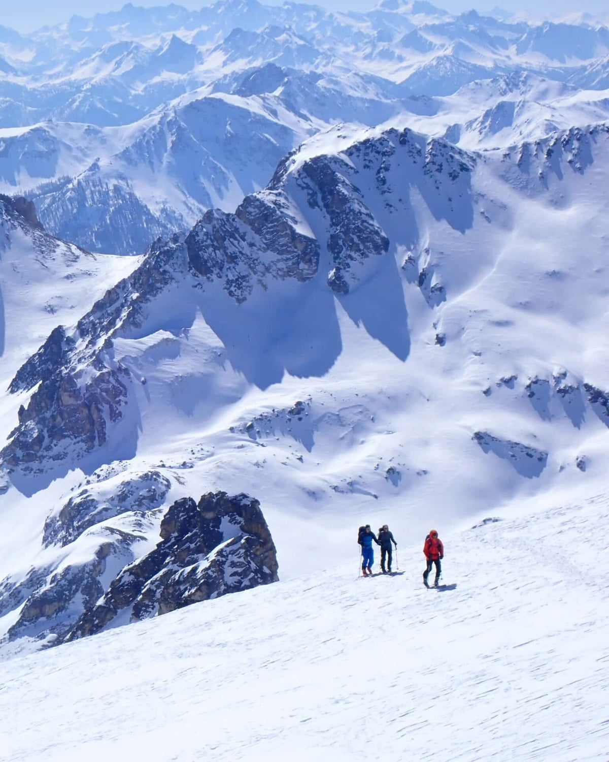 Trois skieurs de randonnée face à un panorama de sommets enneigés