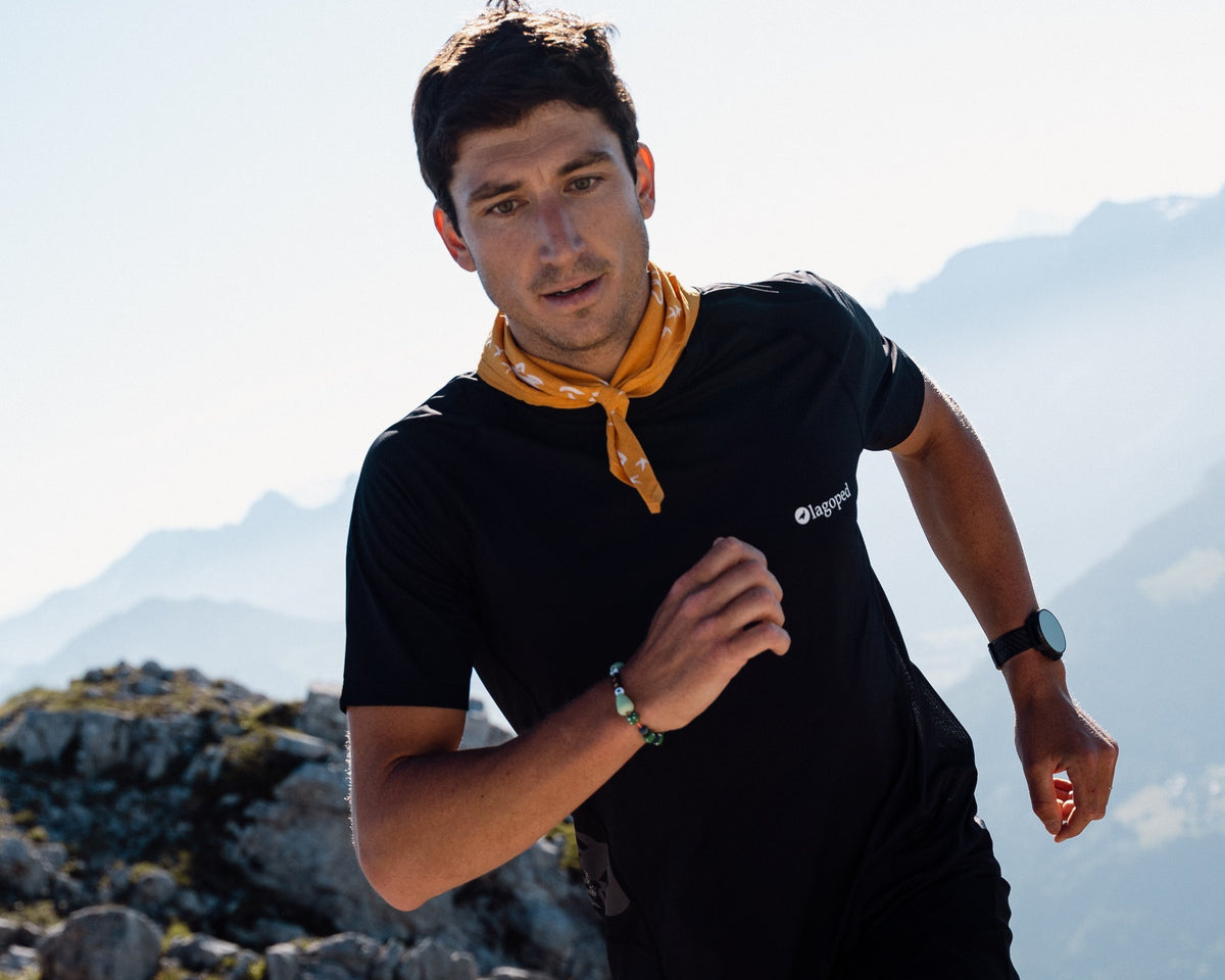 Homme en trail courant sur une crête rocheuse, portant le bandana Lagoped HERON soleil noué autour du cou, en montagne l'été