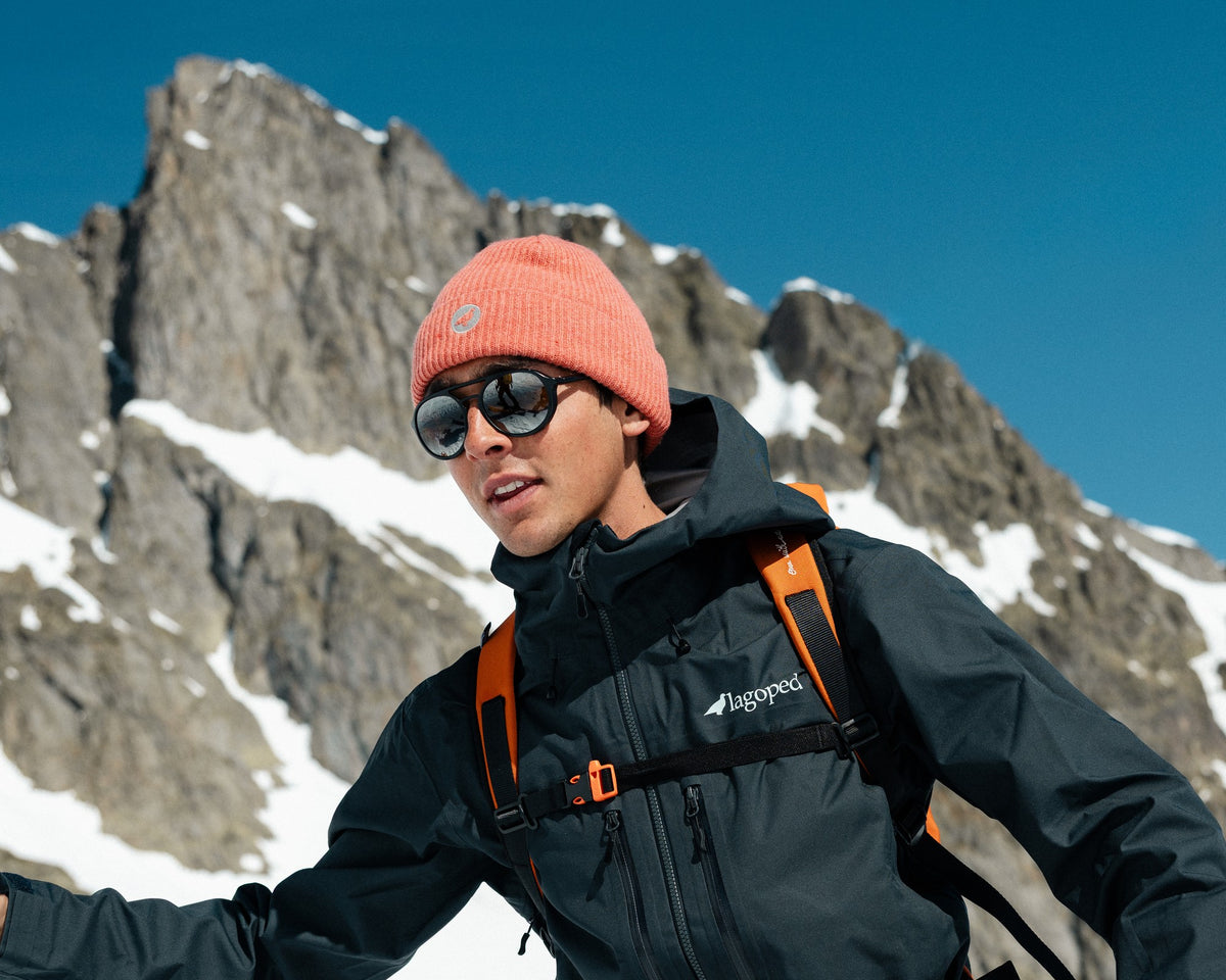 Homme en ski de randonnée avançant bâtons en main sous une arête rocheuse, portant le bonnet en laine Lagoped GEBO RIB ocre