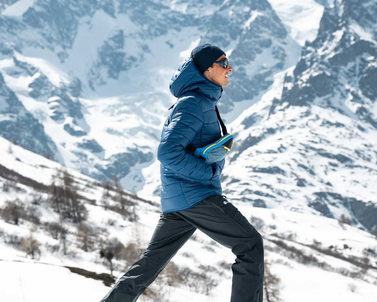 Homme en randonnée hivernale portant la doudoune à capuche Lagoped HEYDO2 Hoodie navy, grande foulée dans la neige face aux glaciers