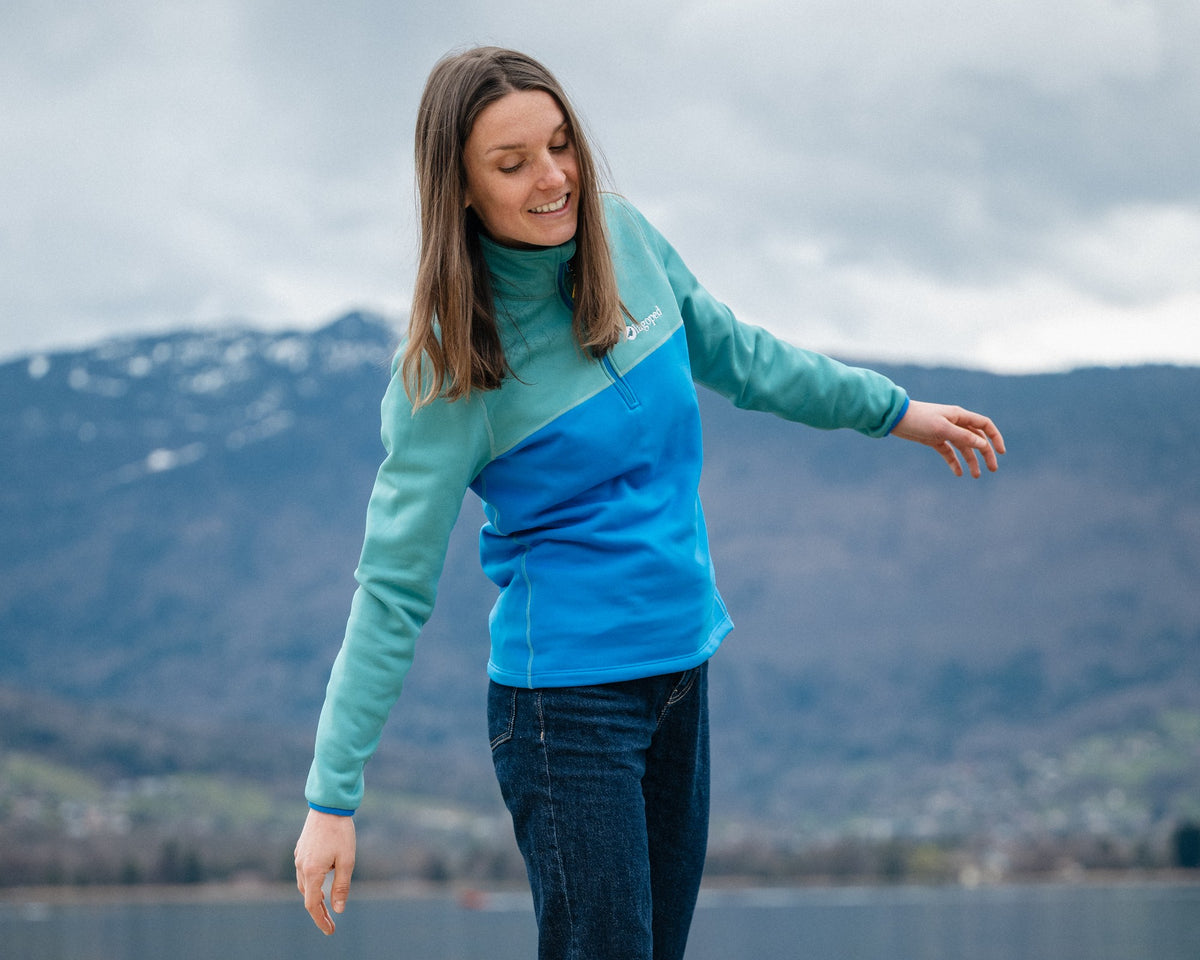 Femme en balade au bord du lac marchant en équilibre sur un muret, portant la micro polaire Lagoped JULEECE bleu roi