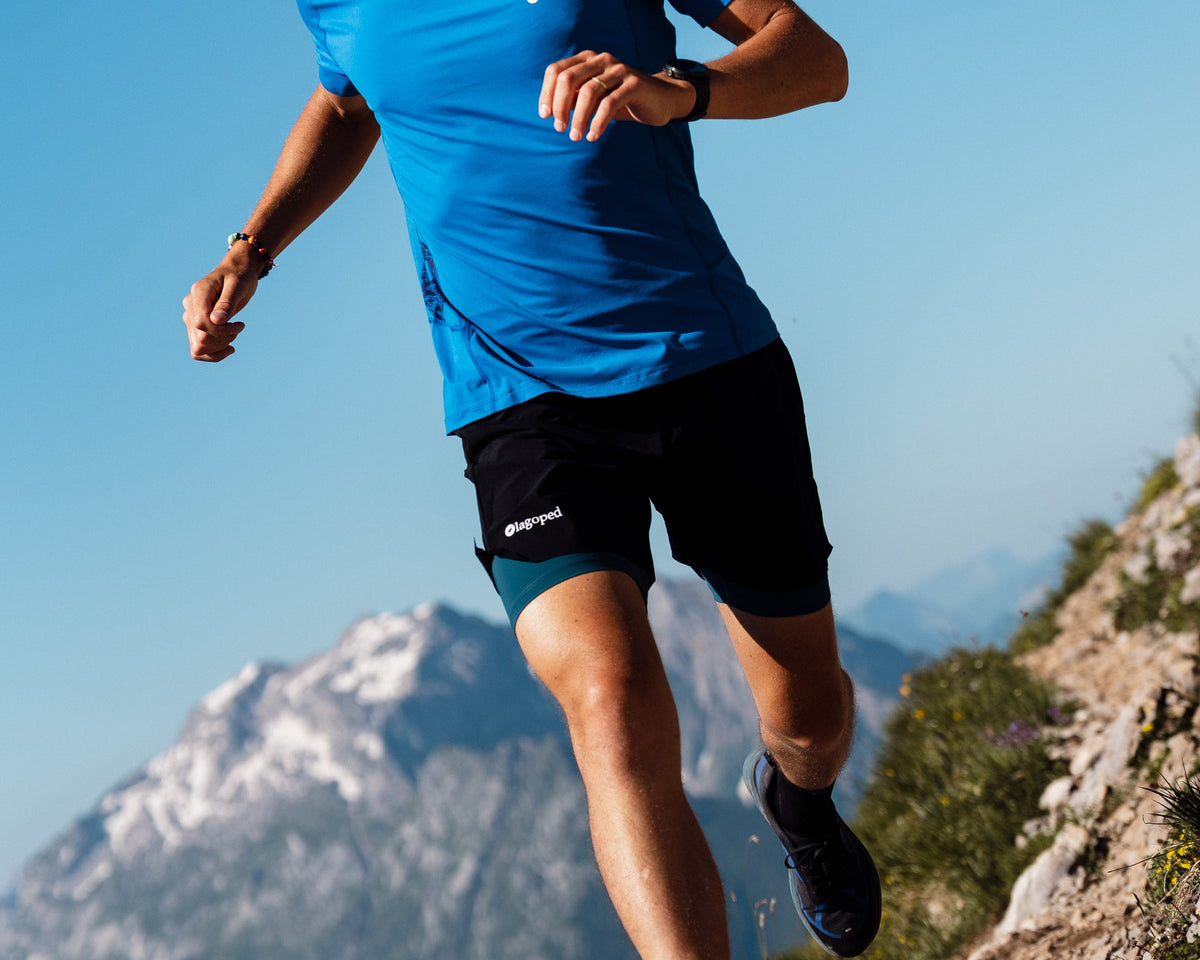 Homme en trail portant le short de trail Lagoped MILVUS bleu sarcelle, descente en pleine foulée sur un sentier de montagne