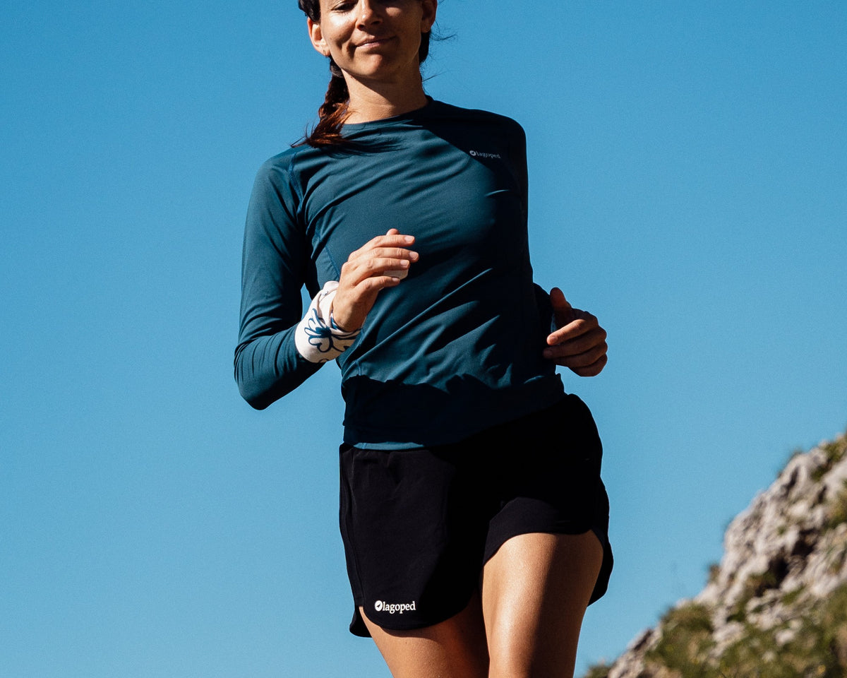 Femme en trail descendant un sentier de montagne en courant, portant le t-shirt technique Lagoped ROKA bleu sarcelle